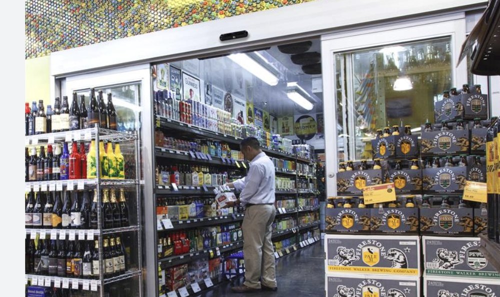 Customer grabbing beer from a beer cave with automatic glass doors