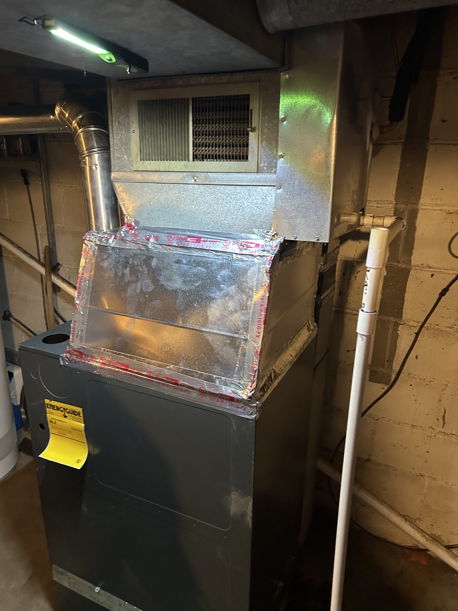 An iced-over A-coil cabinet sitting on a furnace — the frost on the outside of the casing is the giveaway that the coil inside is frozen solid.